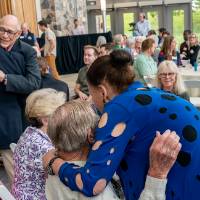 Woman giving hug to gentleman sitting at table at eventT